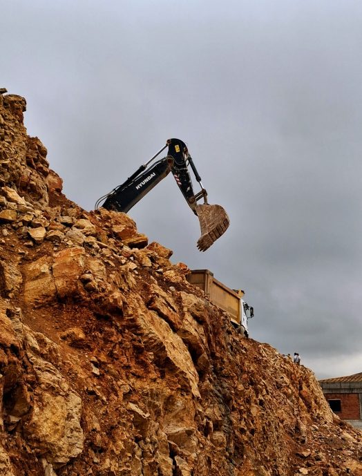 A construction excavator moving rocks at a quarry, captured under cloudy skies.